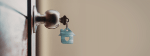 A close-up view of a key inserted in a door lock with a blue house-shaped keyring featuring a heart cutout, symbolising home security and the practical steps involved in keeping your accommodation safe through security measures.